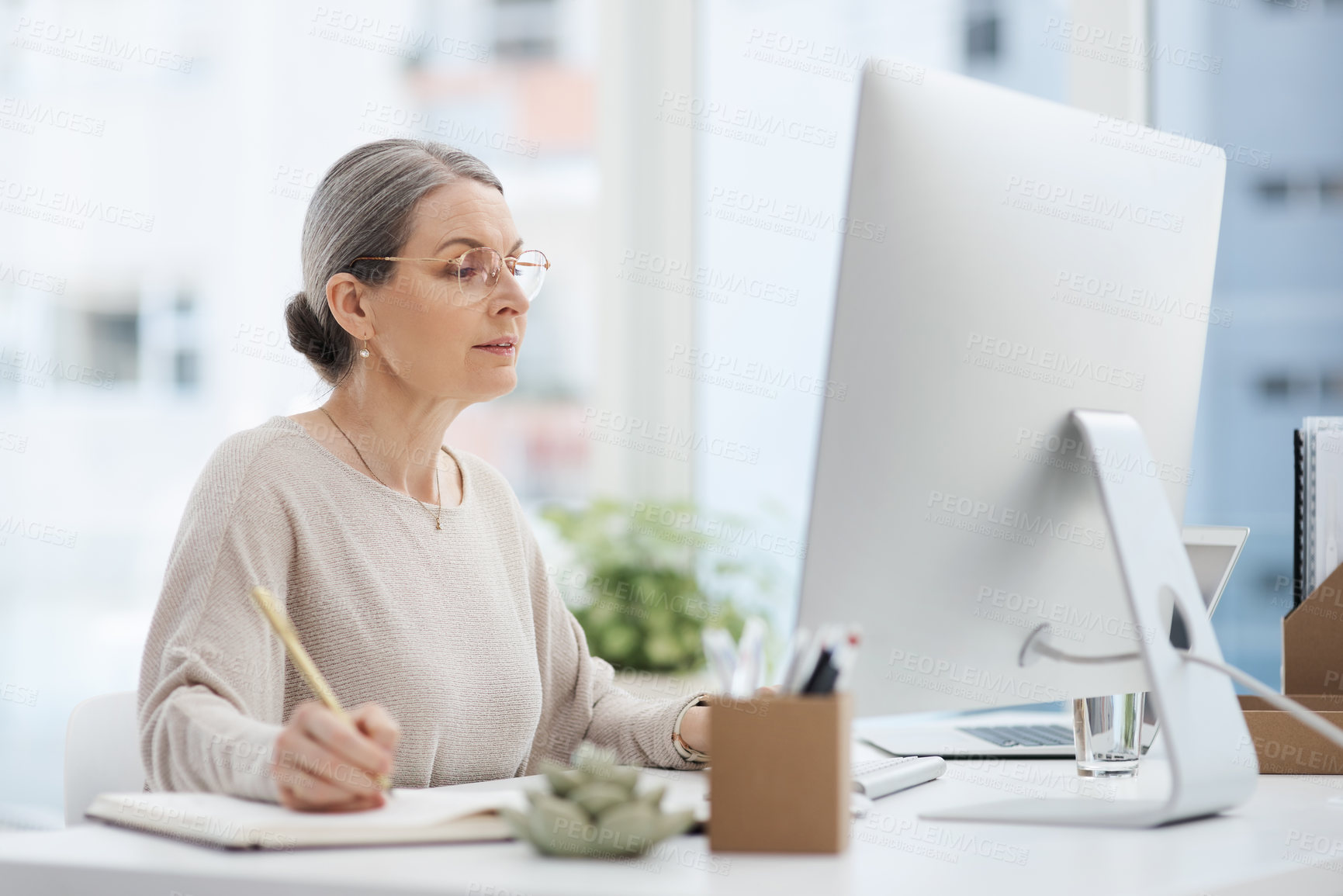 Buy stock photo Cropped shot of an attractive mature businesswoman making notes while working at her desk in the office