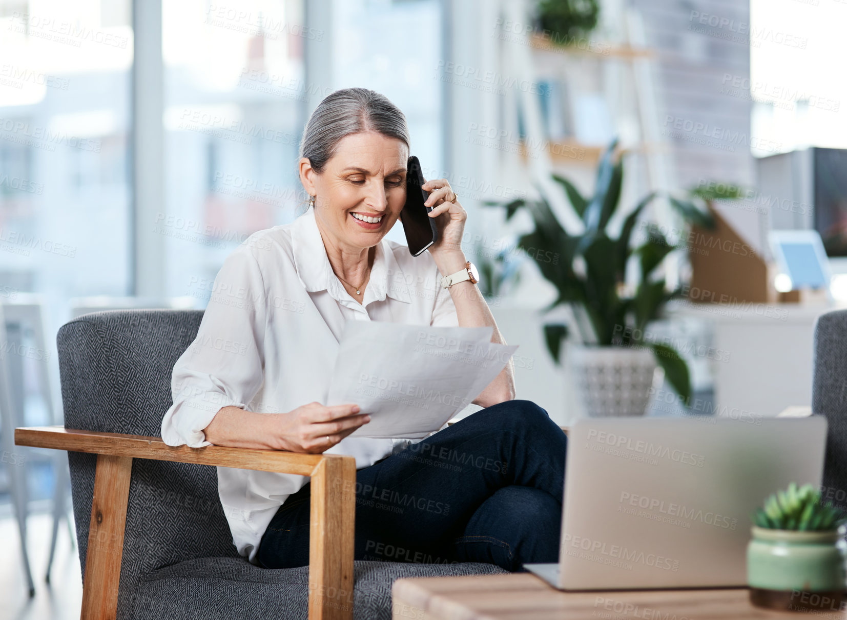 Buy stock photo Shot of a mature businesswoman talking on a cellphone while going through paperwork in an office