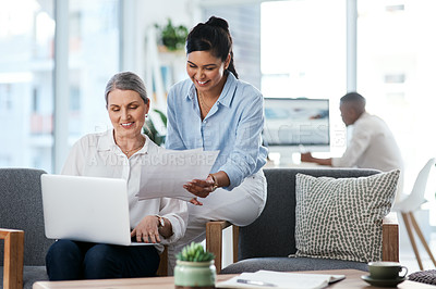 Buy stock photo Shot of two businesswomen going through paperwork while using a laptop together in an office