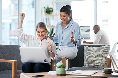Buy stock photo Shot of two businesswomen cheering while working together on a laptop in an office