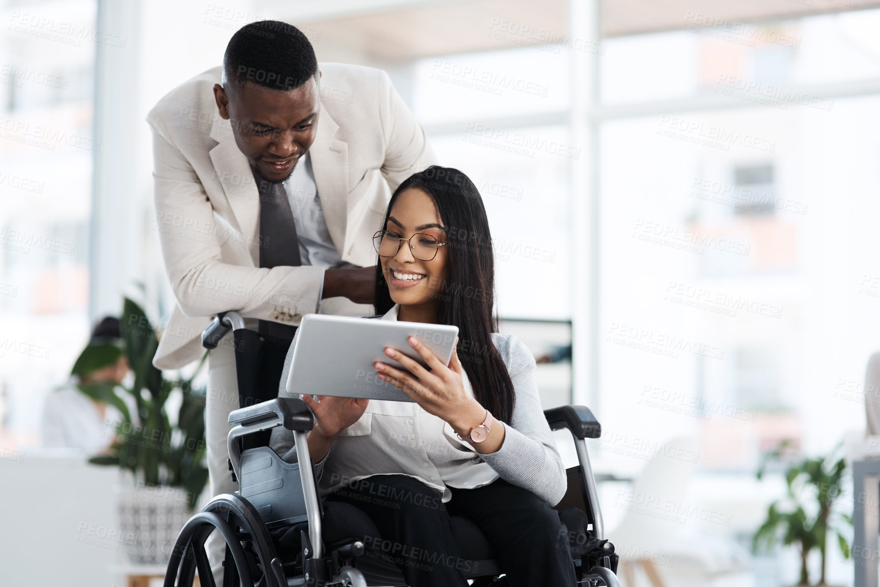 Buy stock photo Cropped shot of an attractive young businesswoman in a wheelchair talking to the male colleague pushing her through the office