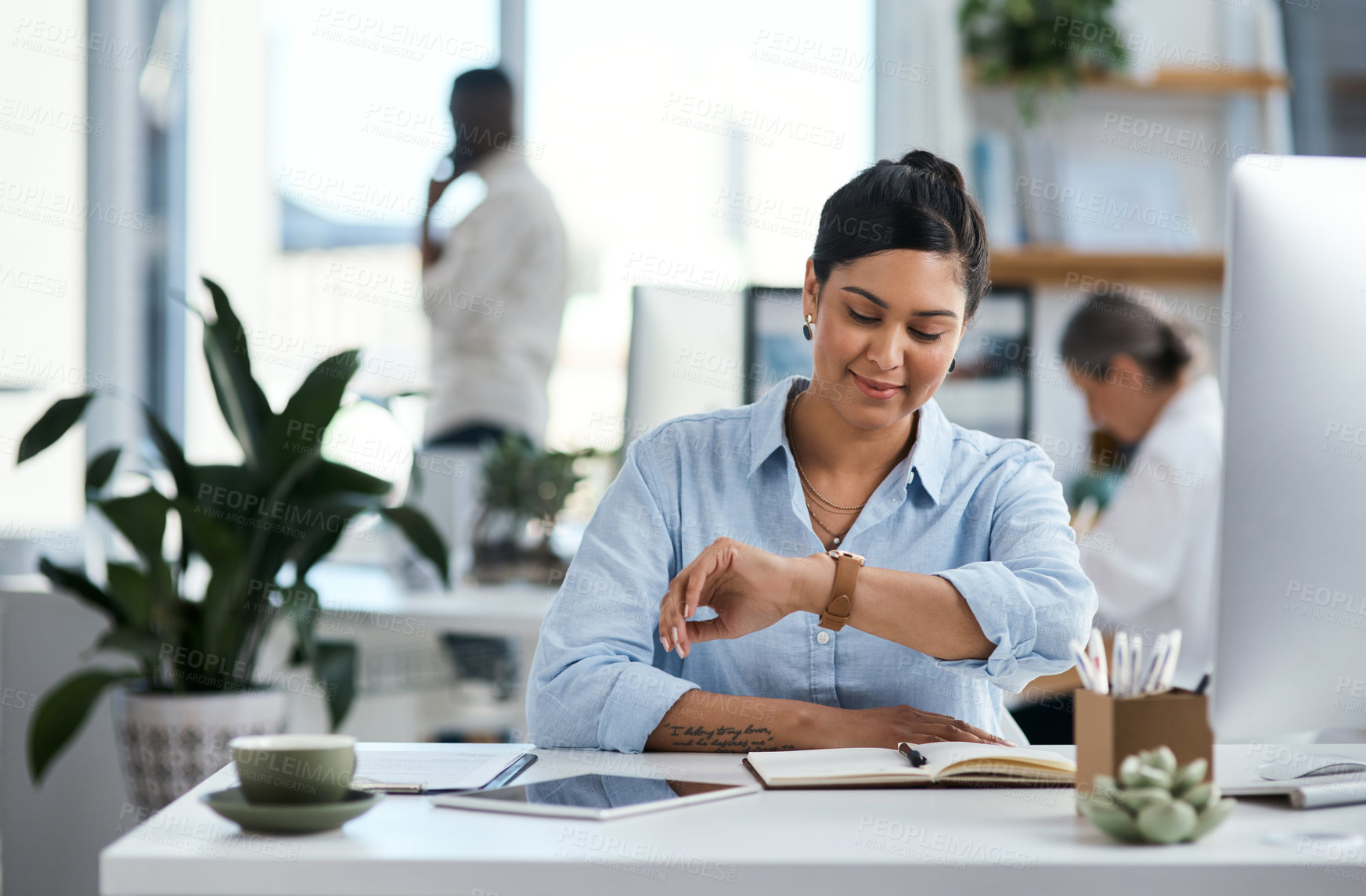Buy stock photo Shot of a young businesswoman checking the time on her wristwatch while working in an office