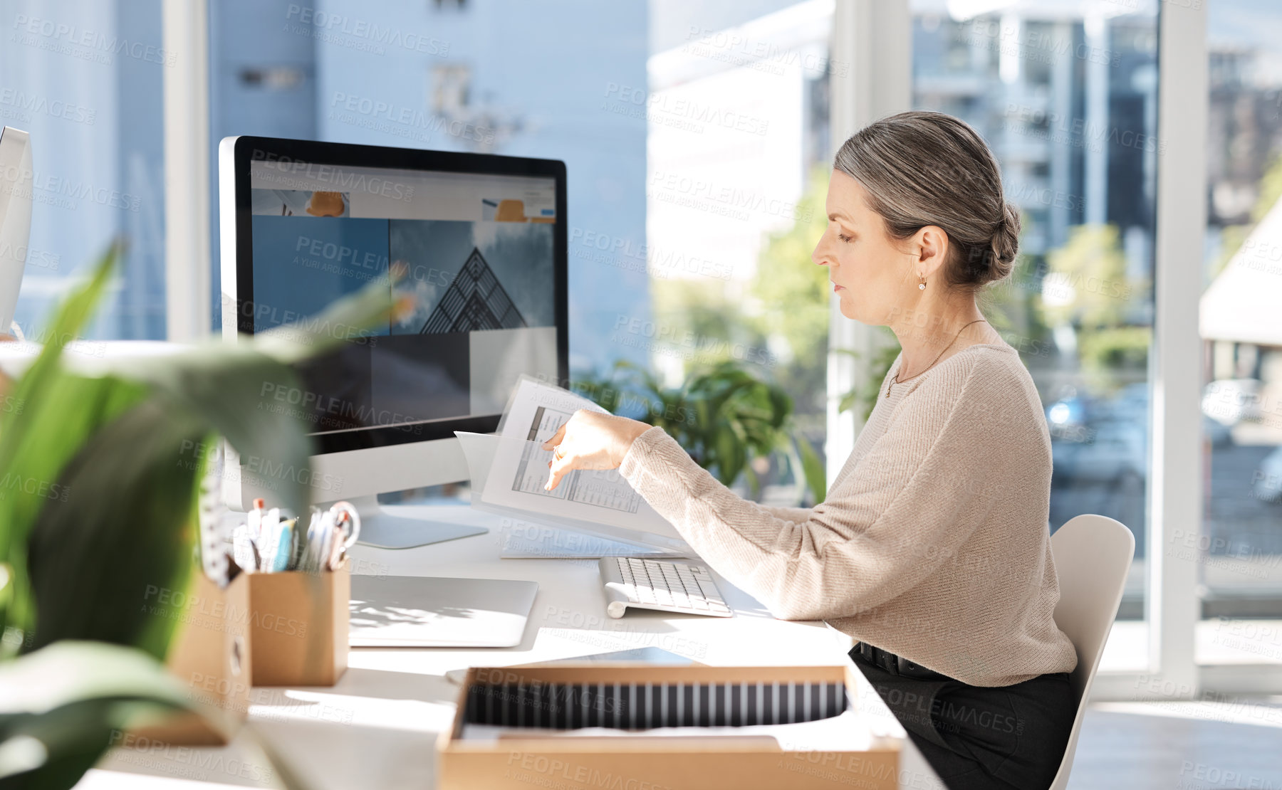 Buy stock photo Cropped shot of an attractive mature businesswoman looking over some paperwork while working at her desk in the office