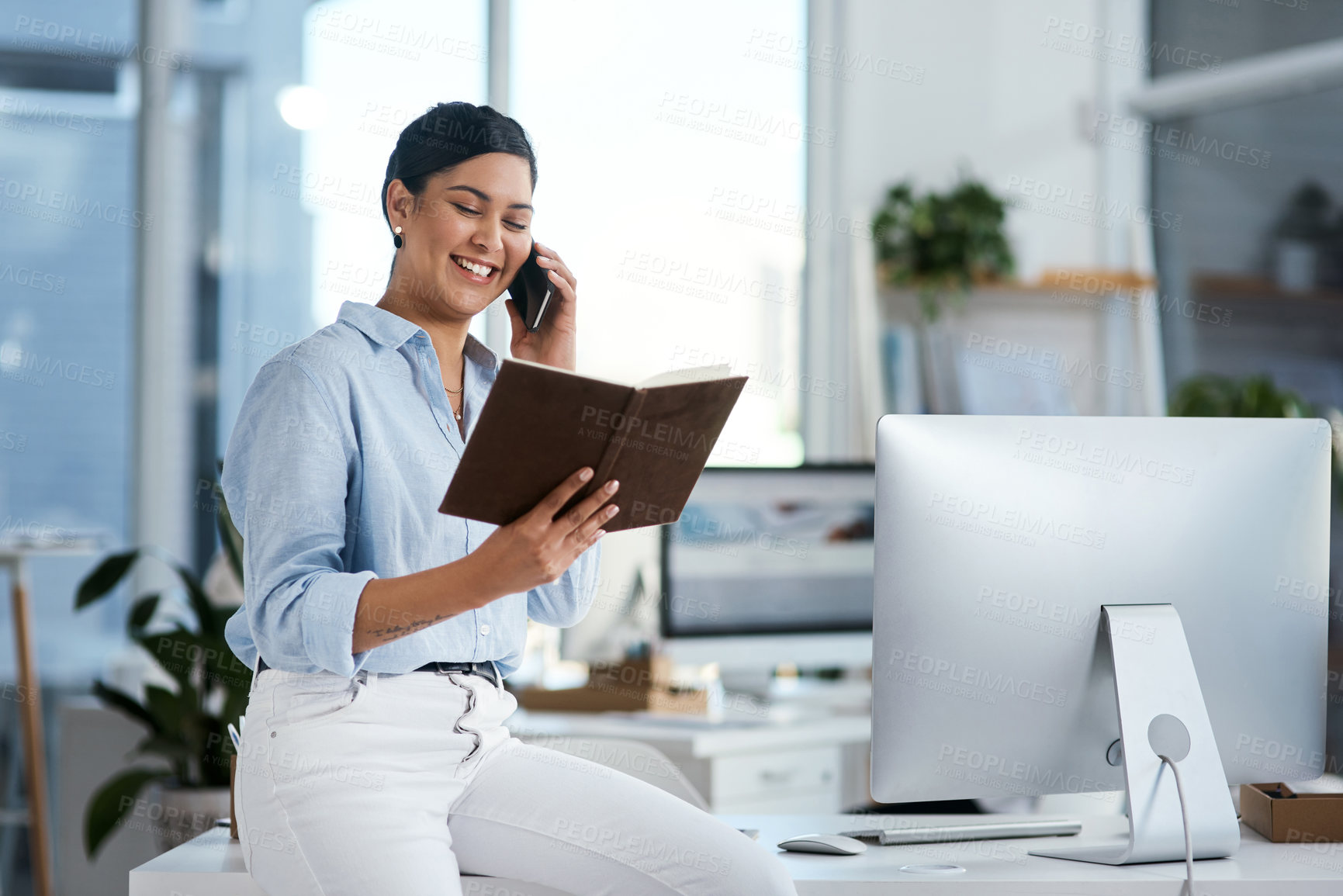 Buy stock photo Shot of a young businesswoman talking on a cellphone while going through notes in an office