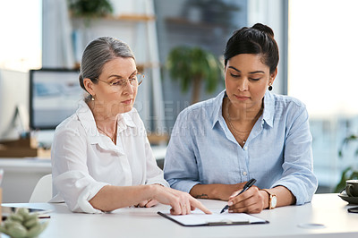 Buy stock photo Shot of two businesswomen going through paperwork together in an office