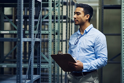 Buy stock photo Shot of a handsome young contractor standing alone in the warehouse and holding a clipboard