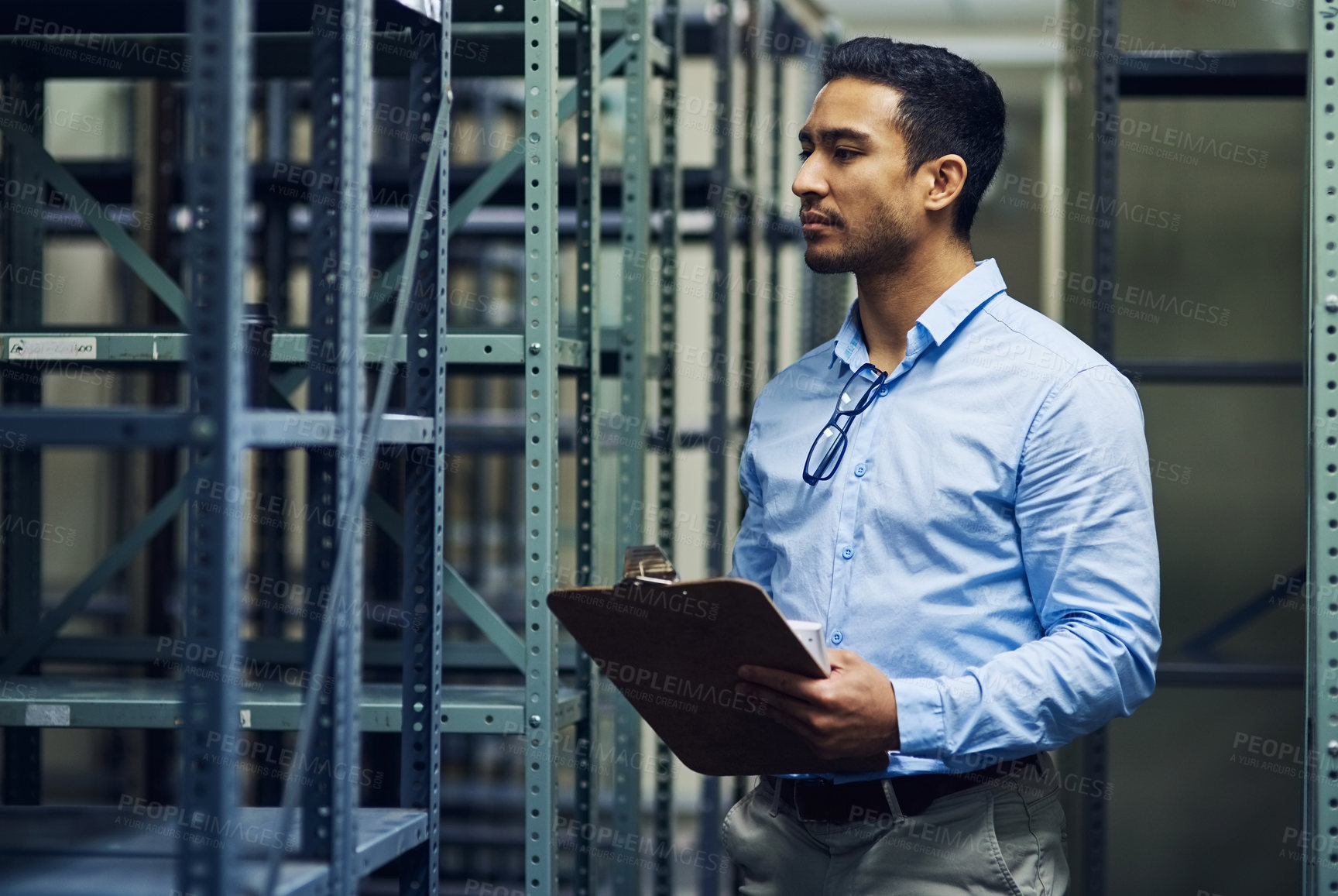 Buy stock photo Shot of a handsome young contractor standing alone in the warehouse and holding a clipboard