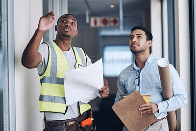 Buy stock photo Shot of two young architects standing together and having a discussion about the room before they renovate