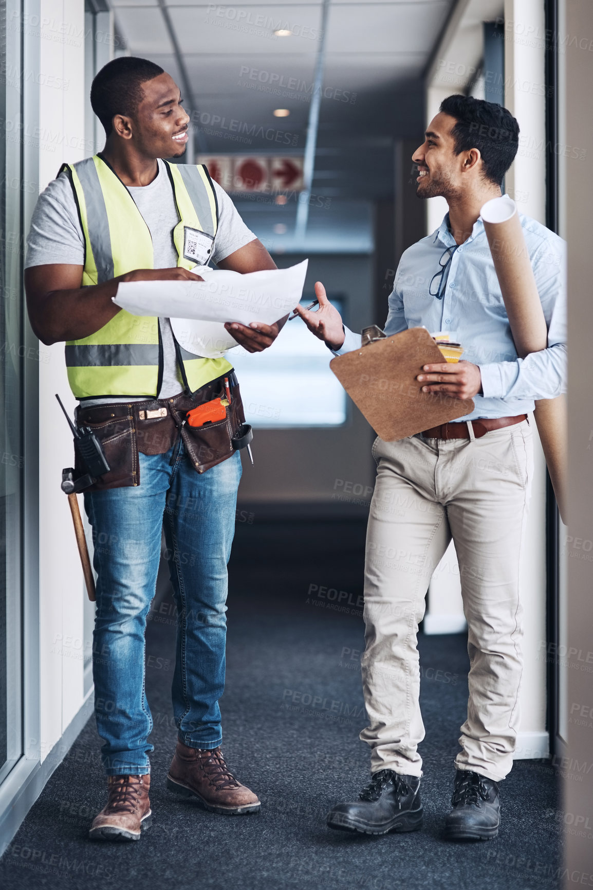 Buy stock photo Shot of two young architects standing together and having a discussion about the room before they renovate