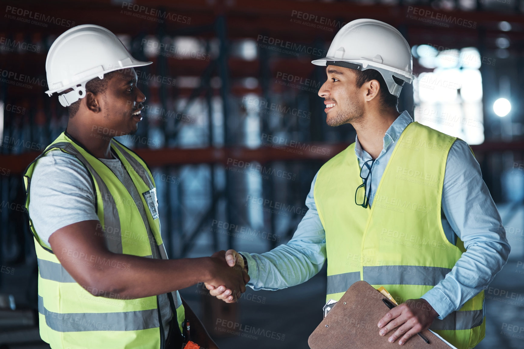 Buy stock photo Shot of two young contractors standing in the warehouse together and shaking hands