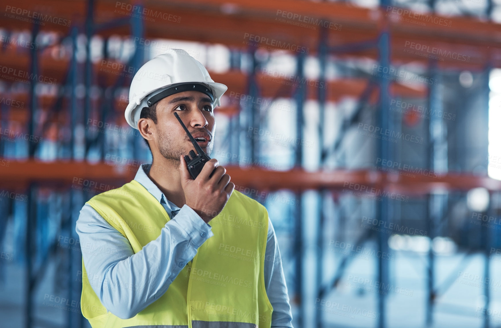 Buy stock photo Shot of a handsome young contractor standing alone in the warehouse and using a walkie talkie