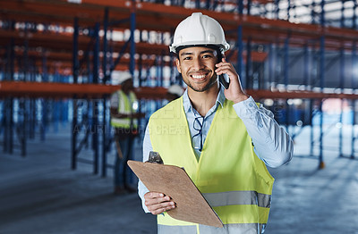 Buy stock photo Shot of a handsome young contractor standing alone in the warehouse and using his cellphone while holding a clipboard