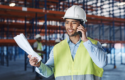 Buy stock photo Shot of a handsome young contractor standing alone in the warehouse and using his cellphone while holding a clipboard
