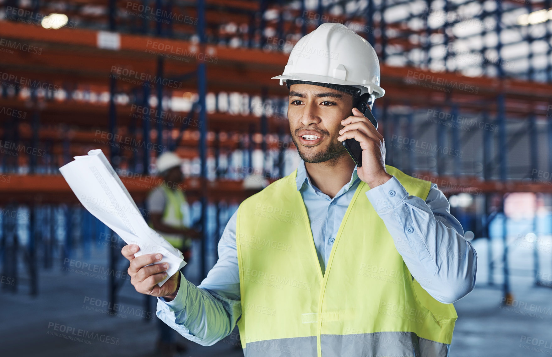 Buy stock photo Shot of a handsome young contractor standing alone in the warehouse and using his cellphone while holding a clipboard