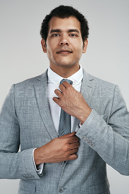 Buy stock photo Studio shot of a businessman adjusting his tie while standing against a grey background