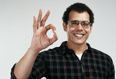 Buy stock photo Shot of a handsome young man showing the ok sign while standing against a grey background