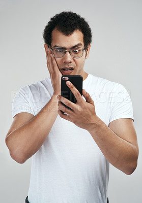 Buy stock photo Shot of a handsome young man using his cellphone while standing against a grey background