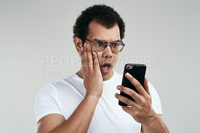 Buy stock photo Shot of a handsome young man using his cellphone while standing against a grey background