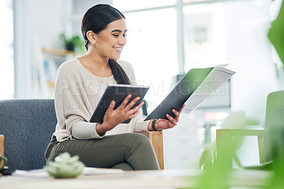 Buy stock photo Shot of a young businesswoman using a digital tablet while going through paperwork in an office