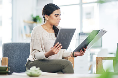 Buy stock photo Shot of a young businesswoman using a digital tablet while going through paperwork in an office