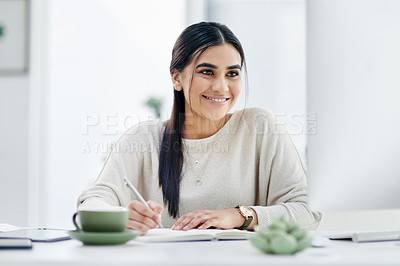 Buy stock photo Shot of a young businesswoman writing notes while using a computer in an an office