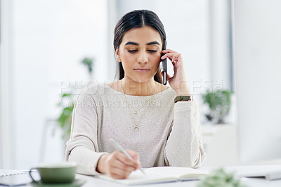 Buy stock photo Shot of a young businesswoman talking on a cellphone while writing notes in an office