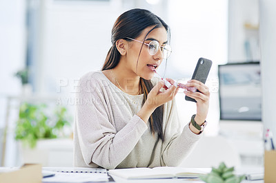 Buy stock photo Shot of a young businesswoman applying lipstick while using her cellphone as a mirror in an office