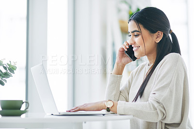 Buy stock photo Shot of a young businesswoman talking on a cellphone while using a laptop in an office