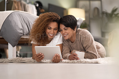 Buy stock photo Shot of a young lesbian couple using a tablet while relaxing in their bedroom