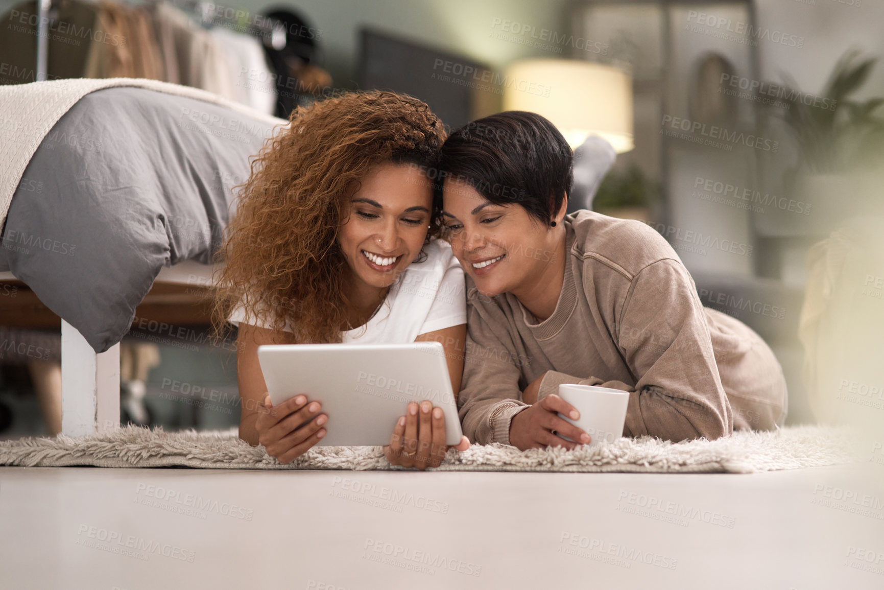 Buy stock photo Shot of a young lesbian couple using a tablet while relaxing in their bedroom