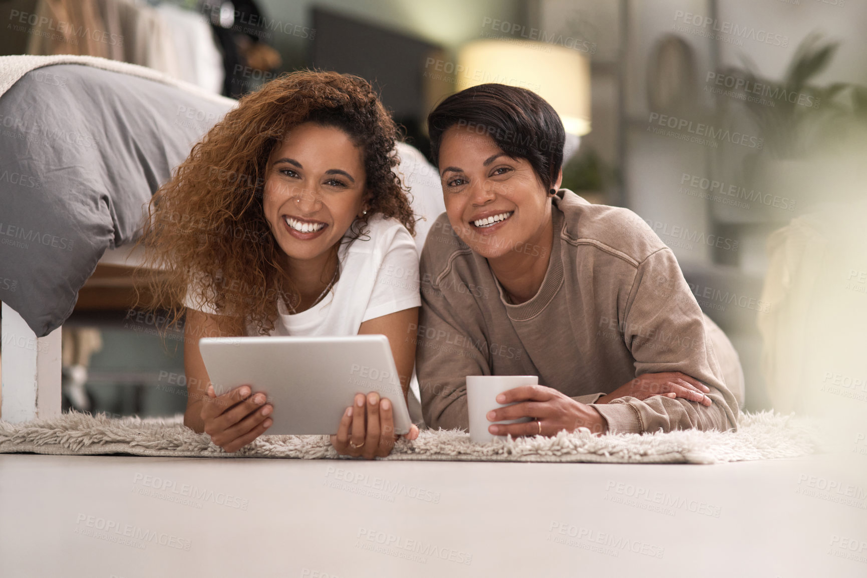 Buy stock photo Shot of a young lesbian couple using a tablet while relaxing in their bedroom