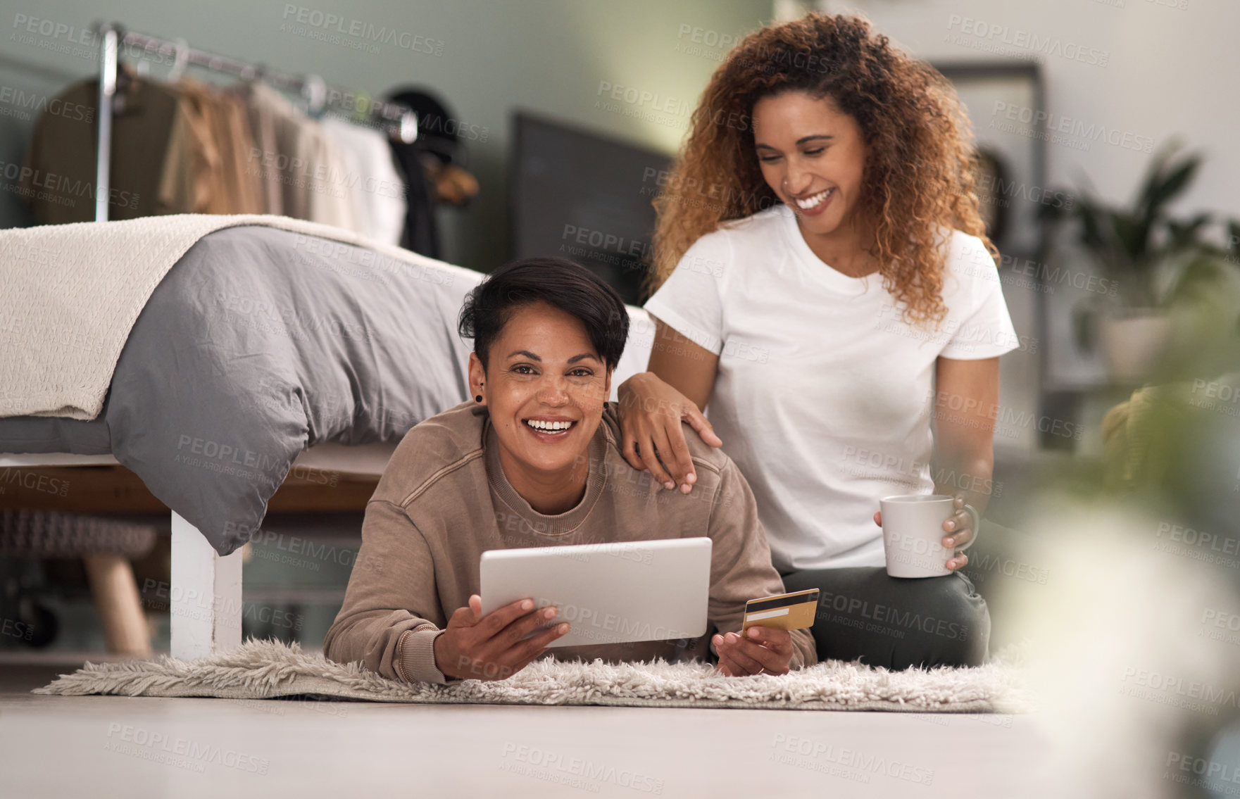 Buy stock photo Shot of a young lesbian couple using a tablet while relaxing in their bedroom