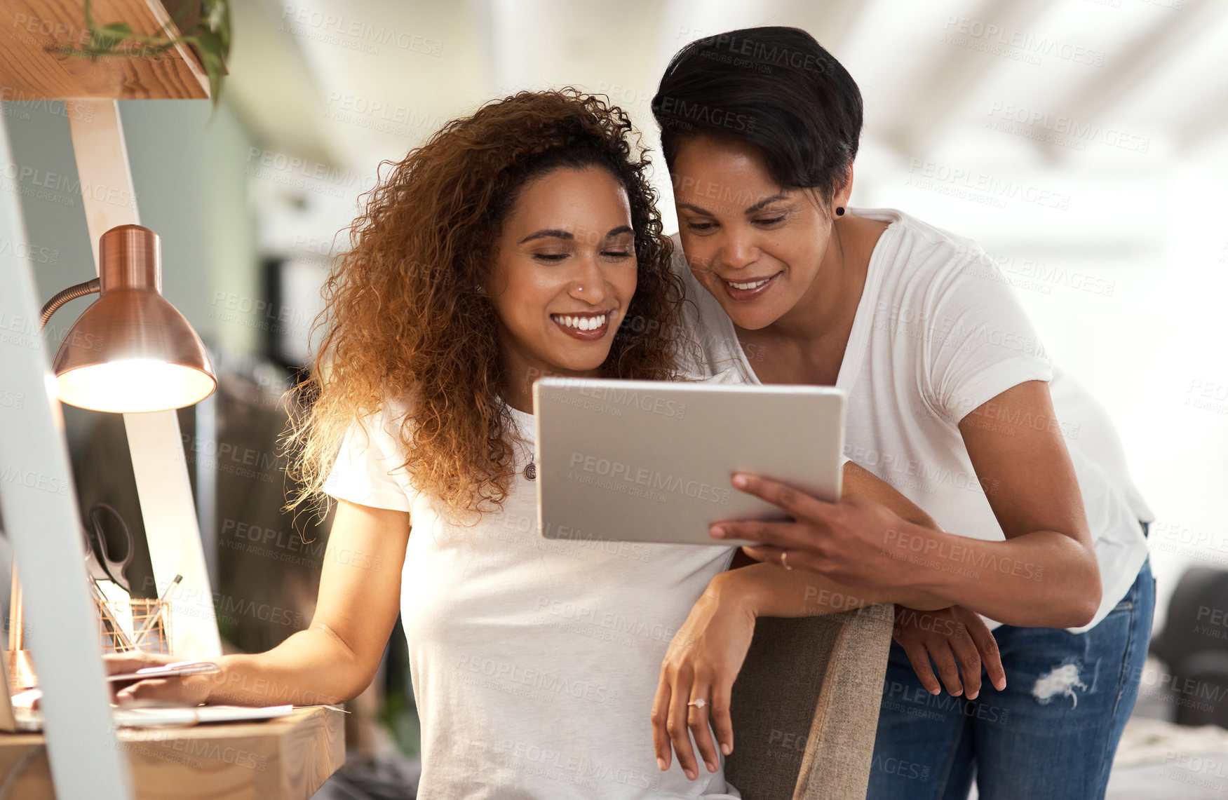 Buy stock photo Shot of a young lesbian couple using a tablet while relaxing in their bedroom