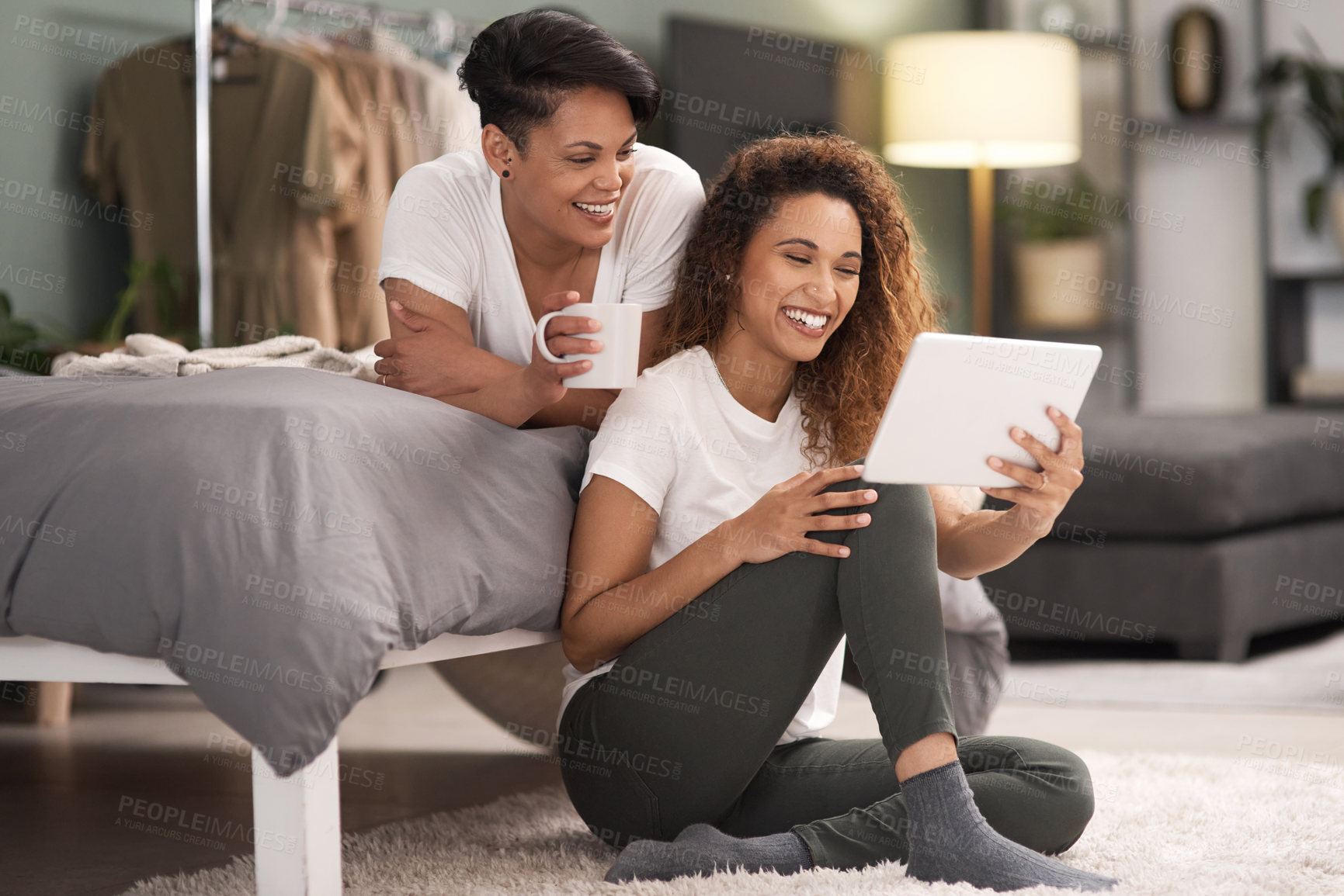 Buy stock photo Shot of a young lesbian couple using a tablet while relaxing in their bedroom