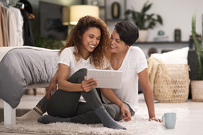 Buy stock photo Shot of a young lesbian couple using a tablet while relaxing in their bedroom