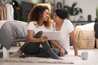 Buy stock photo Shot of a young lesbian couple using a tablet while relaxing in their bedroom