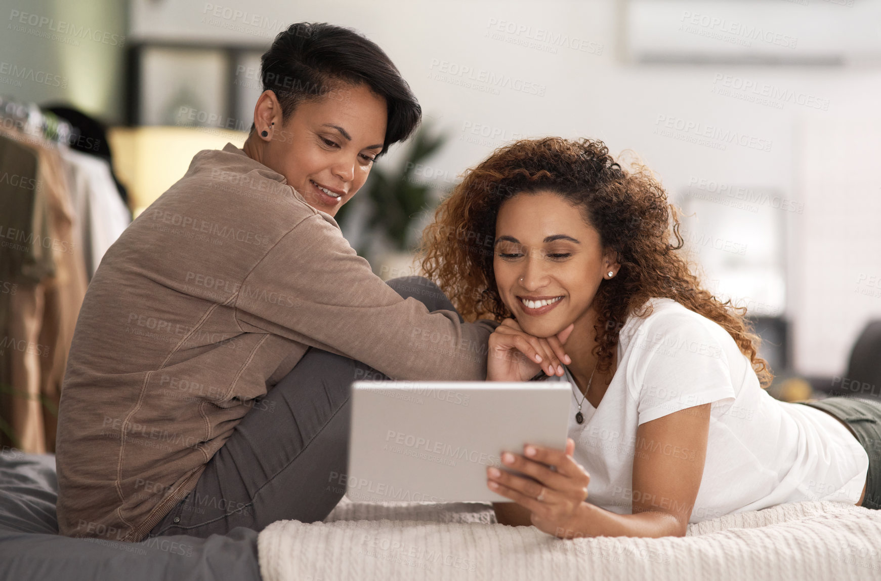 Buy stock photo Shot of a young lesbian couple using a tablet while relaxing in their bedroom