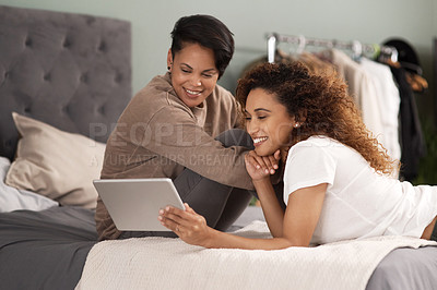 Buy stock photo Shot of a young lesbian couple using a tablet while relaxing in their bedroom