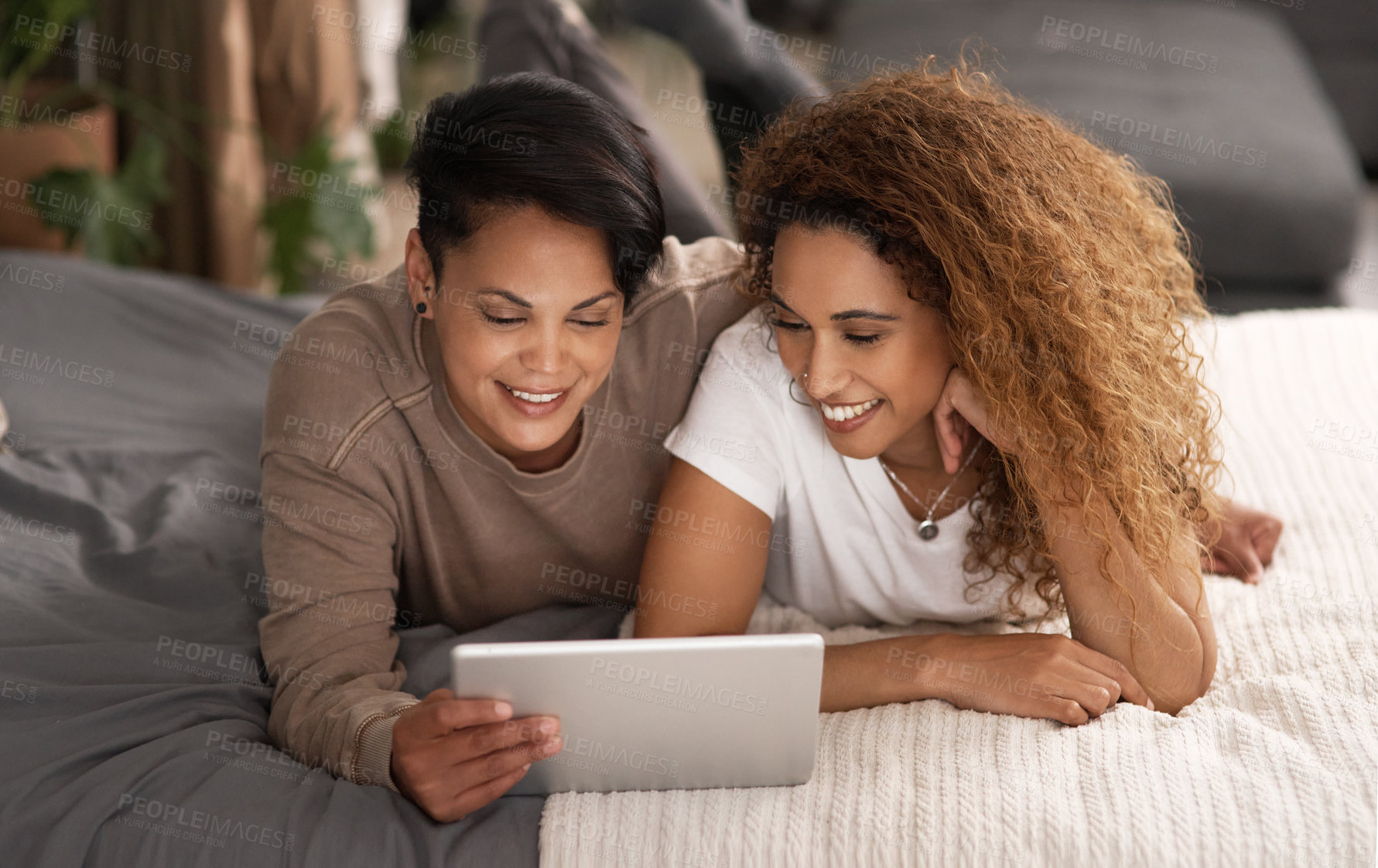 Buy stock photo Shot of a young lesbian couple using a tablet while relaxing in their bedroom