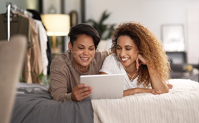 Buy stock photo Shot of a young lesbian couple using a tablet while relaxing in their bedroom