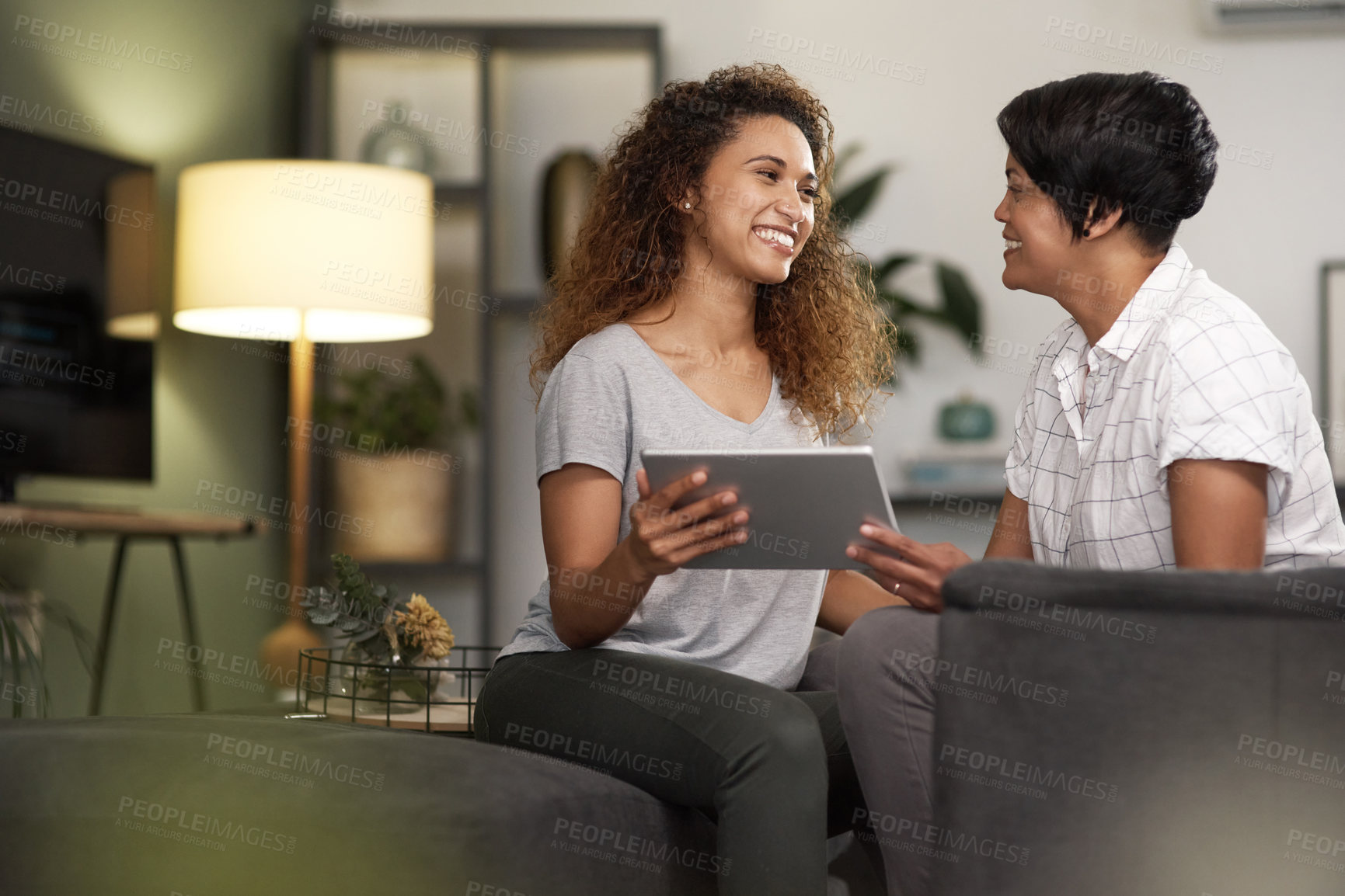 Buy stock photo Shot of a young lesbian couple using a tablet while relaxing in their lounge at home