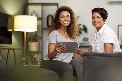 Buy stock photo Shot of a young lesbian couple using a tablet while relaxing in their lounge at home