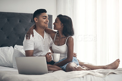 Buy stock photo Shot of a young couple using a laptop while sitting on a bed