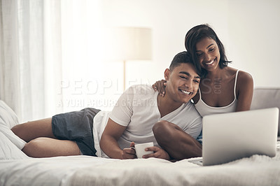 Buy stock photo Shot of a young couple sitting on a bed while using a latop