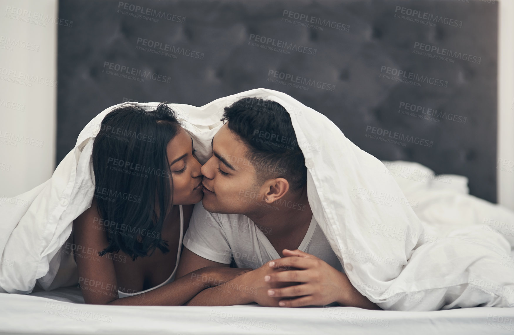 Buy stock photo Shot of a young couple kissing in bed at home