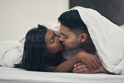 Buy stock photo Shot of a young couple kissing in bed at home