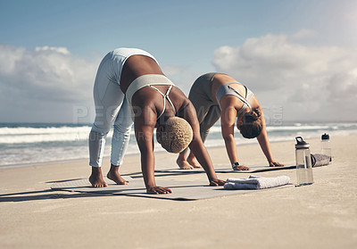 Buy stock photo Shot of two young women practicing yoga on the beach