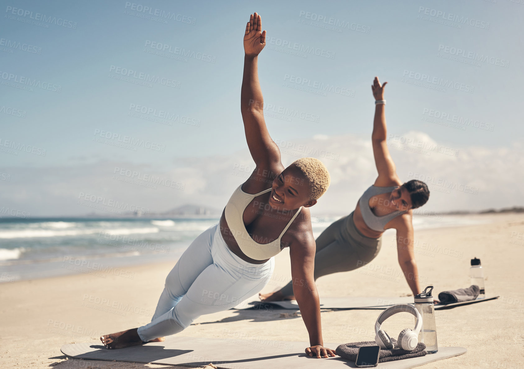 Buy stock photo Shot of two young women practicing yoga on the beach