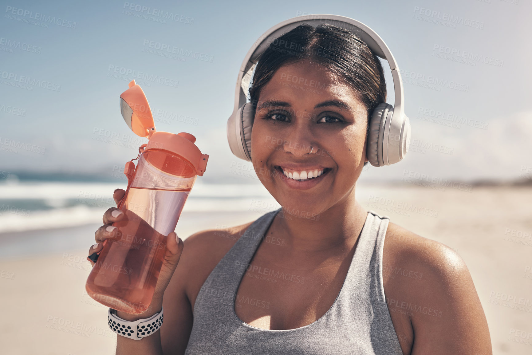 Buy stock photo Shot of a young woman wearing headphones and holding her water bottle while out for a run