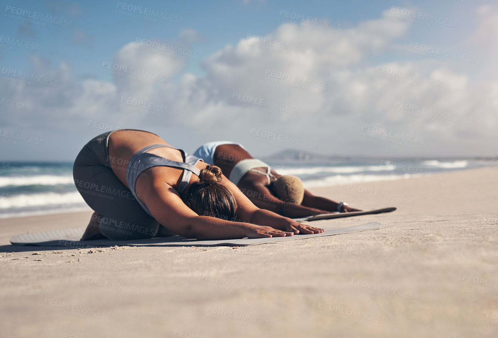 Buy stock photo Shot of two young women practicing yoga on the beach